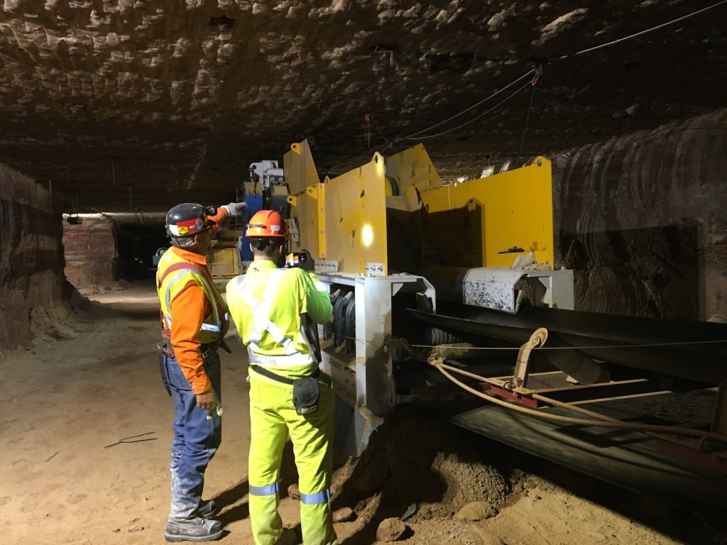 Two workers evaluate the belt drive on a mine's conveyor system.